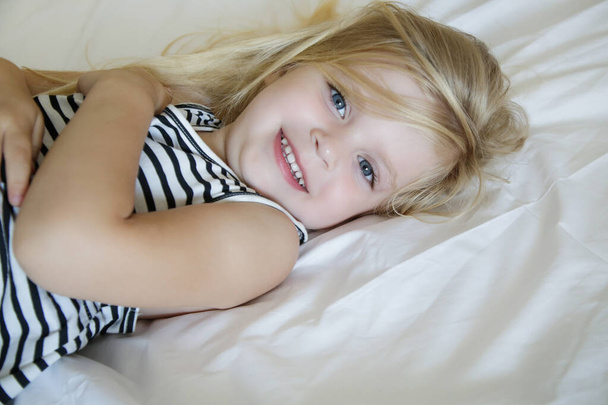 Πορτρέτο του γλυκού κοριτσιού ξαπλωμένη στο κρεβάτι και κοιτάζοντας κάμερα με χαμόγελο στο πρόσωπό της - Φωτογραφία, εικόνα