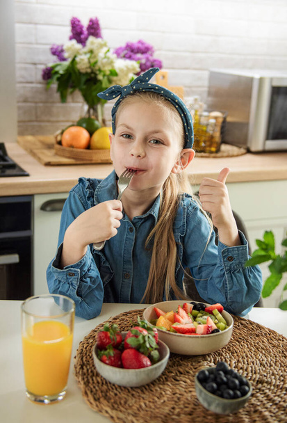 Gesunde Ernährung zu Hause. Nettes kleines Mädchen isst Obstsalat  - Foto, Bild
