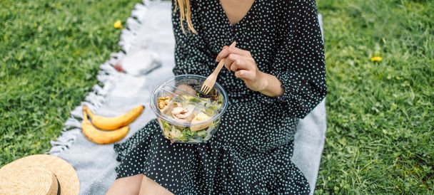 Счастливая женщина держит миску со здоровым салатом и экодеревянной вилкой на зеленом природном фоне. Красивая девушка на пикнике. Концепция питания - Фото, изображение