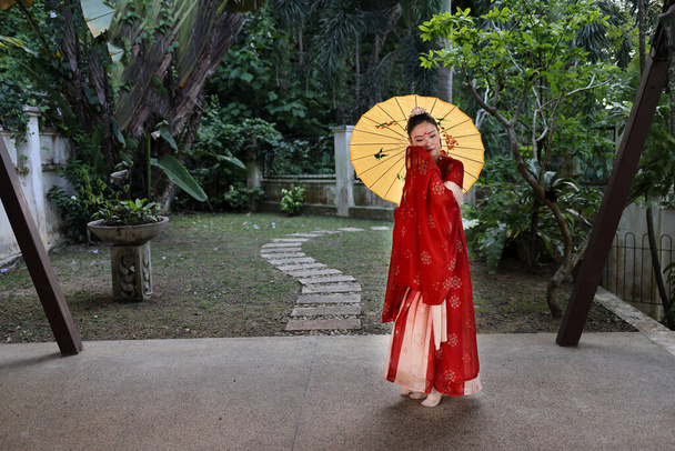 Genç ve çekici Asyalı kadın tadeonal Çinli kırmızı el fu uzun etek giyiyordu. Etek, atkı, saç tokası, açık yeşil bahçe verandasında süslü şemsiye. - Fotoğraf, Görsel
