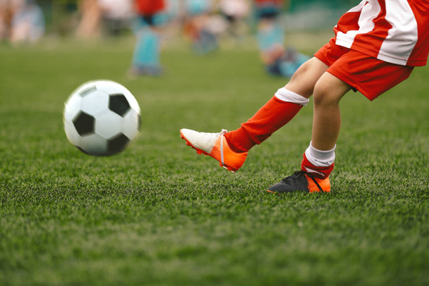 Футболист бьет мячом по траве. Футбольный мяч в действии. Футболист в полосатой красно-белой форме - Фото, изображение