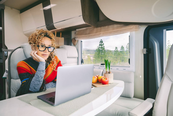 Off grid van het leven en digitale nomade levensstijl. Leuke moderne vrouw die werkt op laptop in een camper met natuur en vrijheid schilderachtige plek buiten het raam. Het leven van slimme werknemers - Foto, afbeelding
