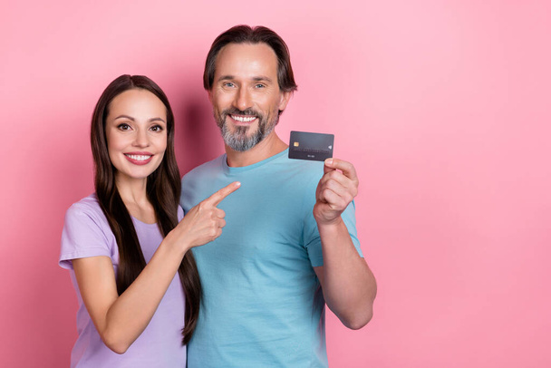 Photo of two satisfied nice people indicate finger debit plastic card isolated on pink color background. - Foto, Imagem