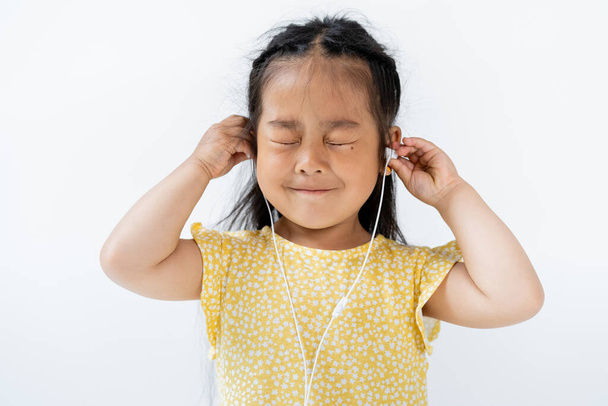 complacido chica asiática con los ojos cerrados usando auriculares con cable aislado en gris  - Foto, Imagen