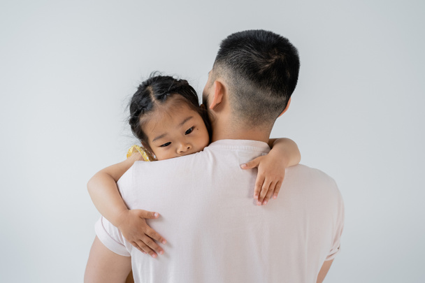 back view of father with beard holding in arms asian preschooler daughter isolated on grey  - Photo, Image