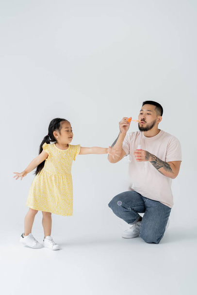 asiatique père souffler savon bulles près joyeux préscolaire fille sur gris - Photo, image