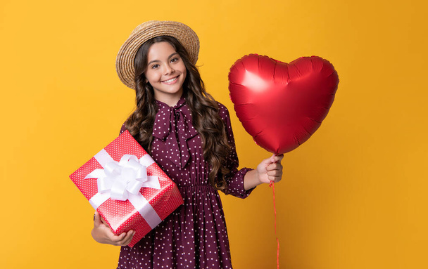 happy teen girl with red heart balloon and present box on yellow background. - Foto, Imagen