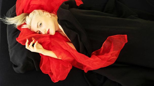 Şehvetli, baştan çıkarıcı seksi bir moda portresi yaslanmış seksi bir genç kadın, model, yatağa uzanmış, siyah ve kırmızı kumaşa sarılmış, kumaş, kopyalama alanı. - Fotoğraf, Görsel