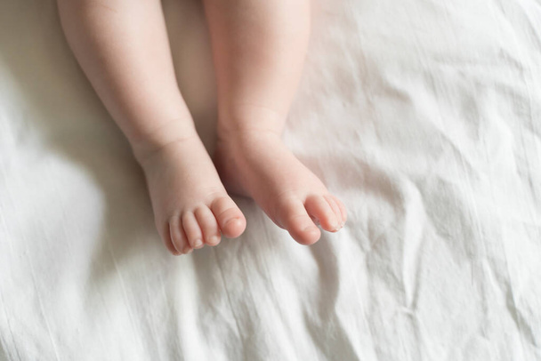 Pies de bebé sobre el fondo blanco de la cama. Cuidado, paternidad, concepto de protección. Foto de alta calidad - Foto, imagen