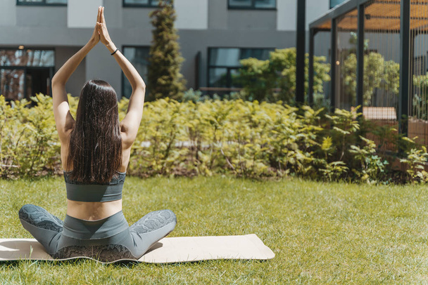 Mujer en yoga posan al aire libre en parque o jardín. Una esbelta chica europea se dedica a la práctica del yoga indio para la curación y el desarrollo del cuerpo en el clima soleado de verano. Sanidad - Foto, imagen