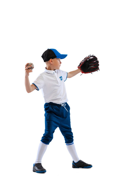 Little boy, baseball player, pitcher in blue-white uniform training isolated on white studio background. Concept of sport, achievements, studying, competition. Copy space for ad, vertical composition - 写真・画像