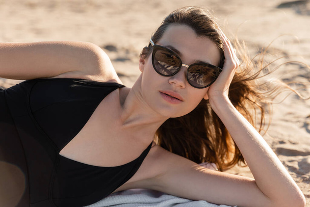 jovem mulher em óculos de sol elegantes deitado em cobertor na praia de areia  - Foto, Imagem
