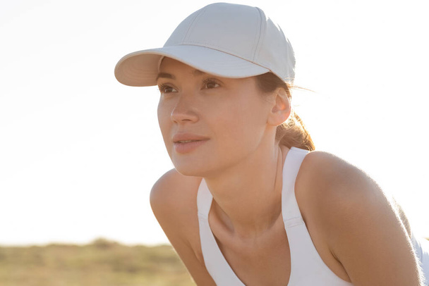 brunette young woman in baseball cap and sports bra looking away  - Foto, Imagem