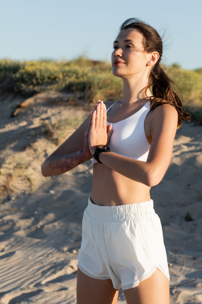 молодая женщина в шортах и спортивном бюстгальтере медитирует на пляже летом - Фото, изображение