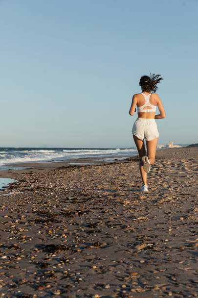 back view of sportive woman in white shorts jogging near sea in summer - Foto, immagini