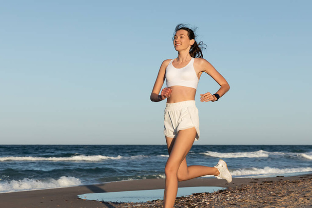 夏には海の近くでスポーツウェアのジョギングをしている若い女性を笑顔 - 写真・画像