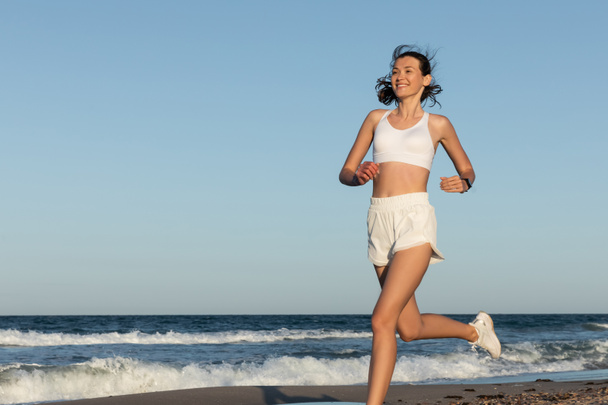 cheerful young and sportive woman jogging near sea in summer - Foto, imagen