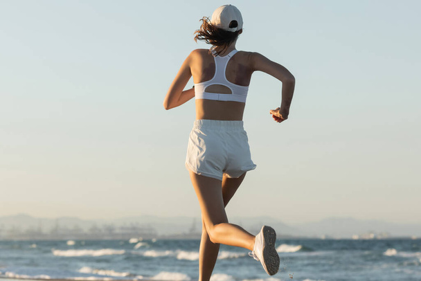 terug uitzicht op jonge sportieve vrouw rennen in de buurt van de zee in de zomer - Foto, afbeelding
