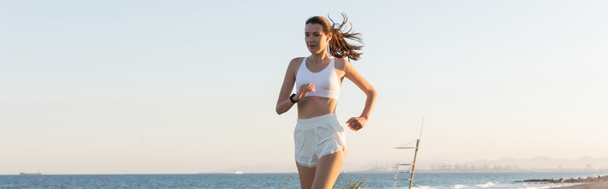 jeune femme en short et écouteurs sans fil jogging près de la mer, bannière - Photo, image