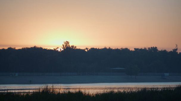 Спокійний помаранчевий захід сонця на прекрасному ставку. Мальовничий пейзаж жовте небо над водними болотами. Темний силует пишний ліс освітлений м'яким сонячним світлом. Дике природне середовище тихе озеро
.  - Фото, зображення
