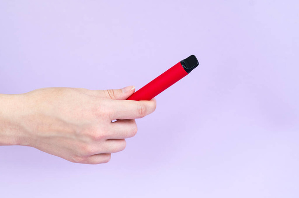 Cigarro eletrônico descartável de diferentes sabores na mão em um fundo violeta claro. O conceito de tabagismo moderno - Foto, Imagem