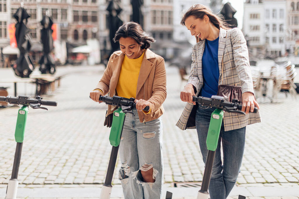 eスクーターを使用して市内中心部の幸せな2つのファッショナブルな女性の友人 - 写真・画像