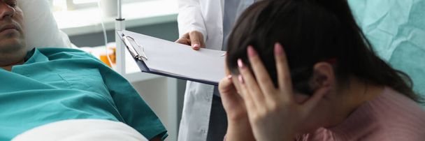 Arzt mit Dokumenten vor weinender Ehefrau und Patientin im Krankenhauszimmer. Unterstützung des Konzepts der unheilbaren Patienten - Foto, Bild