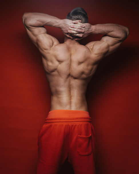 Muskulöser männlicher Rücken mit Händen hinter dem Kopf. Der athletische junge Mann zeigt seine kräftigen Muskeln auf dem Rücken. Rücken des Bodybuilders auf rotem Hintergrund im Studio. Hände hinter dem Kopf. - Foto, Bild