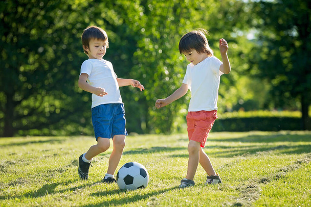Two cute little kids, playing football together, summertime. Children playing soccer outdoor - Zdjęcie, obraz