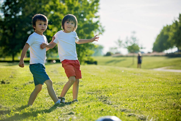 Two cute little kids, playing football together, summertime. Children playing soccer outdoor - Foto, imagen