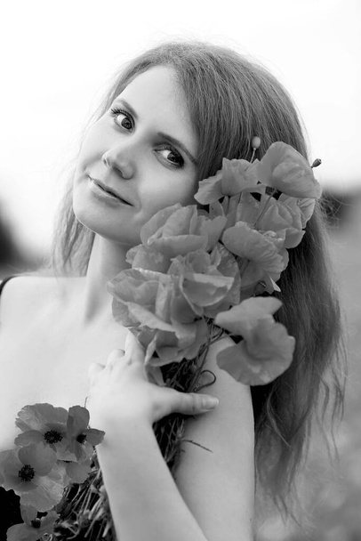 Stunning black and white portrait of a beautiful young redhead woman in a black sundress  holding bouquet of red poppies. Flowers. Summer.  Fashion and beauty concept.  - Фото, зображення