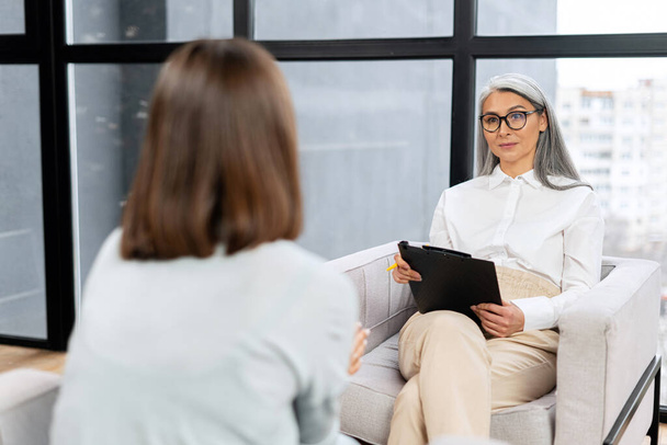 Senior grey haired therapist expresses support and empathy to a upset female patient during therapy session. Mental health concept - Foto, Imagen