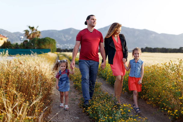 Onnellinen perheen isä äiti ja kaksi tytärtä sisaret kävely maaseudulla luonto auringonlaskun aikana.Huoleton vanhemmat hauskaa lastensa kanssa kentällä. - Valokuva, kuva