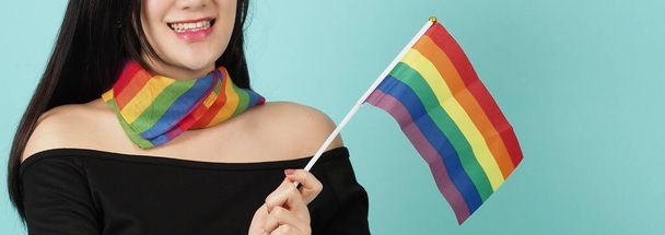 LMBTQ nő kezében büszkeség zászló áll szemben a kék zöld háttér. Ázsiai LMBTQ nő szivárvány sállal a nyakán. okosnak és energikusnak tűnik. LMBTQ sokszínűségi büszkeség koncepció. - Fotó, kép