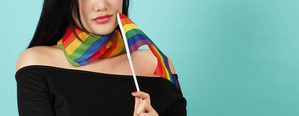 Kobieta LGBTQ z flagą dumy stojąca na niebieskim zielonym tle. Azjatka LGBTQ z tęczowym szalikiem na szyi. wyglądają inteligentne jasne i energiczne wesoły. Koncepcja dumy różnorodności LGBTQ. - Zdjęcie, obraz