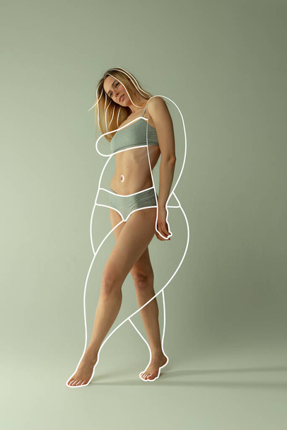 Jonge mooie vrouw in innerlijke slijtage met perfecte lichaamsvorm en witte lijnen rond het lichaam voor het verliezen van gewicht geïsoleerd over groene achtergrond. Concept van gezond eten, dieet, gewicht, fitness, reclame - Foto, afbeelding