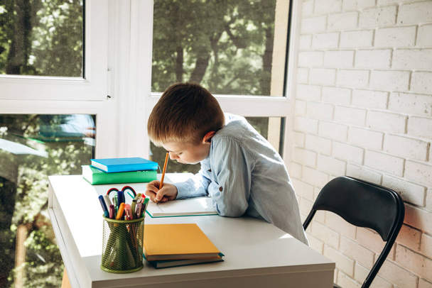 A schoolboy writes numbers in a notebook at a white desk. Back to school concept - Foto, immagini