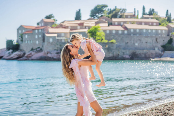 Mother and daughter tourists on background of beautiful view St. Stephen island, Sveti Stefan on the Budva Riviera, Budva, Montenegro. Travel to Montenegro concept. - Fotó, kép