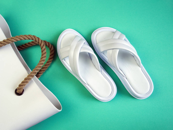 Zapatillas blancas de verano para mujer y una bolsa de goma blanca con asas marrones sobre fondo negro. Zapatillas. Imagen horizontal - Foto, imagen