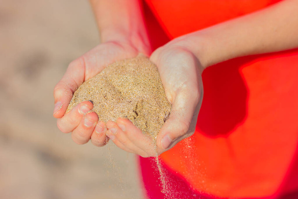 közeli kép egy maroknyi homok a kezében egy fiatal nő a háttérben a tengerparton. - Fotó, kép
