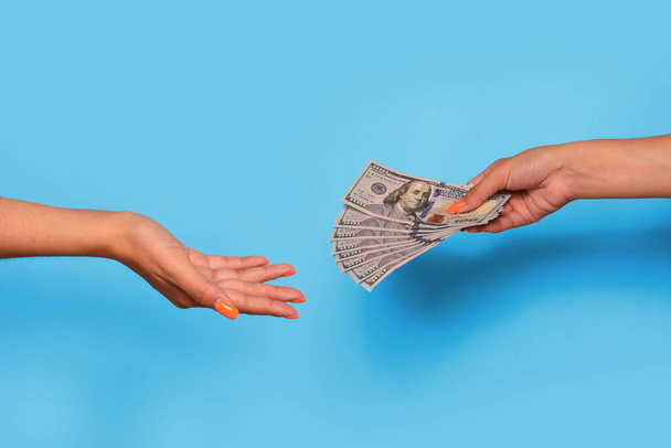 Hand gibt Dollar-Währung und Hand nehmen, über blauem Hintergrund. Geld geben, um zu helfen. Hochwertiges Foto - Foto, Bild