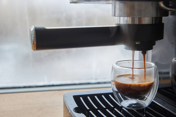 Frischen Kaffee aus der Espressomaschine zubereiten. Espresso in transparenter Kaffeetasse herstellen. - Foto, Bild