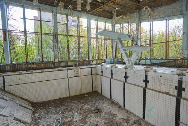 Piscina abandonada en Pripyat. Gimnasio destruido en una ciudad radiactiva. La calle está cubierta de árboles y arbustos. Tampón saltarín
. - Foto, Imagen