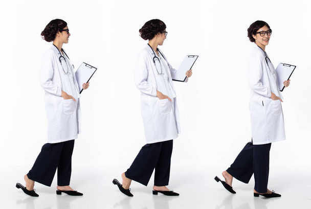 Повна довжина 30-х років 40-х Азійська жінка-доктор з стетоскопом, ходячи вперед зліва направо, носіть формальні туфлі. Самка з лікарні "Посмішка" несе таблицю "Пацієнт" на білому фоні. - Фото, зображення
