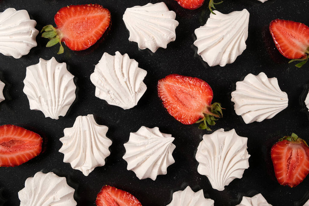 Meringue blanche aux fraises sur fond noir, vue de dessus. Dessert sucré de sucre et blanc d'oeuf aux fruits. - Photo, image