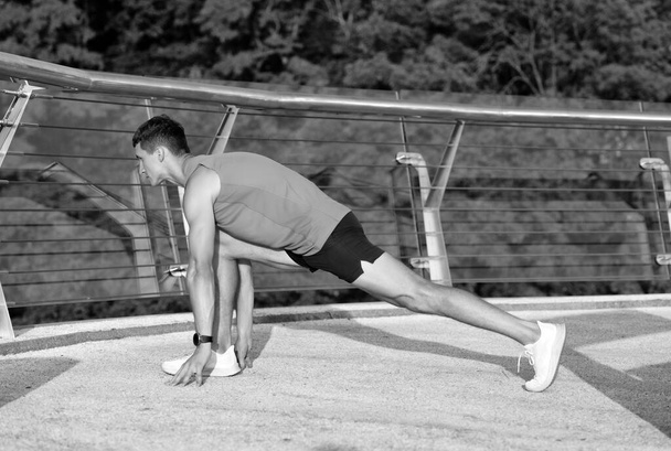 Sportman houden longpositie doen stretch routine na outdoor atletische training op de promenade, stretching. - Foto, afbeelding