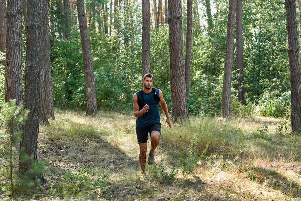 Young caucasian sportsman running or jogging in green forest. Handsome bearded dark-haired athletic man wearing sportswear. Concept of modern healthy lifestyle. Sunny summer daytime - Foto, imagen