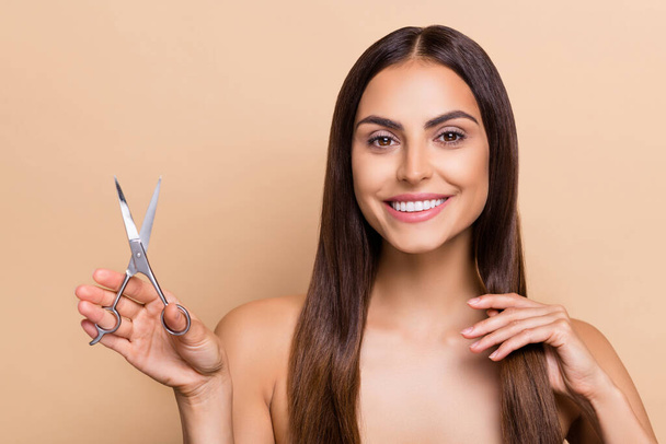 Portrait of attractive cheery healthy long-haired girl holding scissors making style isolated over beige pastel color background. - Photo, image