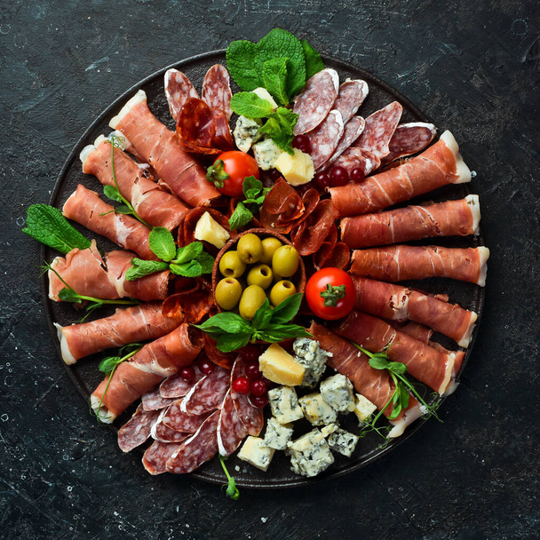 Italian prosciutto, dried pork, parmesan cheese, olives and snacks on a plate. Top view. On a gray stone background. - Photo, image