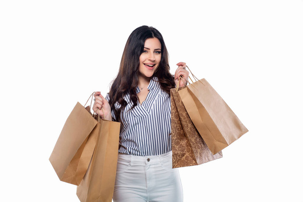 Krásná brunetka kavkazský mladý dívka v bílých kalhotách a pruhované košile drží nákupní tašky izolované na bílém pozadí - Fotografie, Obrázek
